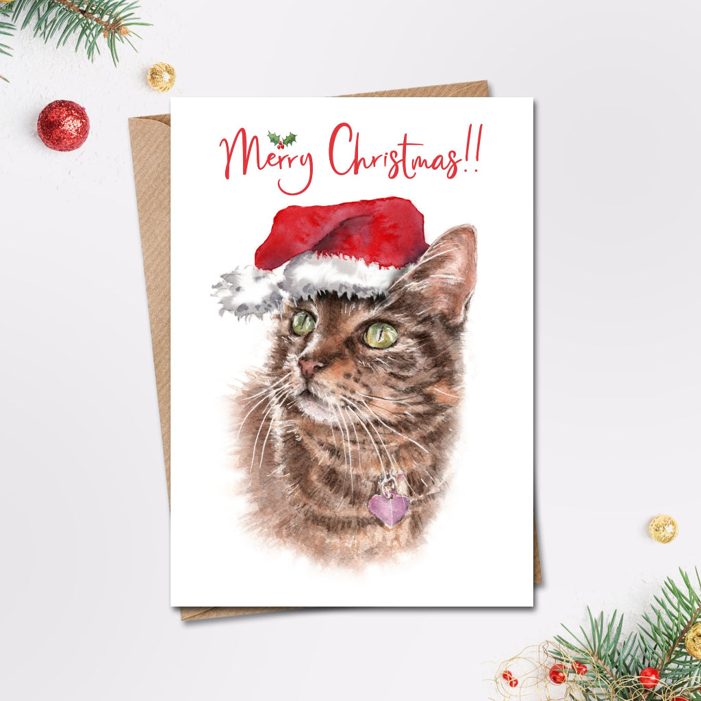 Merry christmas card with beautiful realistic painting of short haired tabby cat in a santa hat on the front