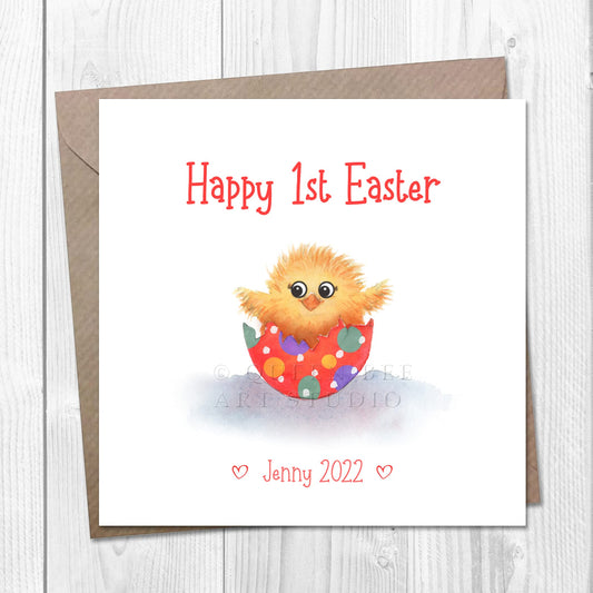 A personalised 1st Easter card with a cute illustration of a chick in a colorful egg, with the text 'Happy 1st Easter' and a name 'Jenny' printed on the front. The card is accompanied by a brown Kraft envelope.