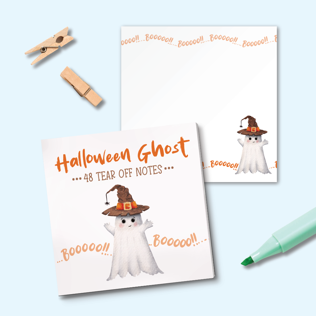 Halloween-themed tear-off notes shown in a styled flat lay with two white note pads featuring a ghost in a witch hat, orange 'Halloween Ghost' text, and 'Boo!' accents, plus wooden clothespins and a mint marker on a pale blue background.