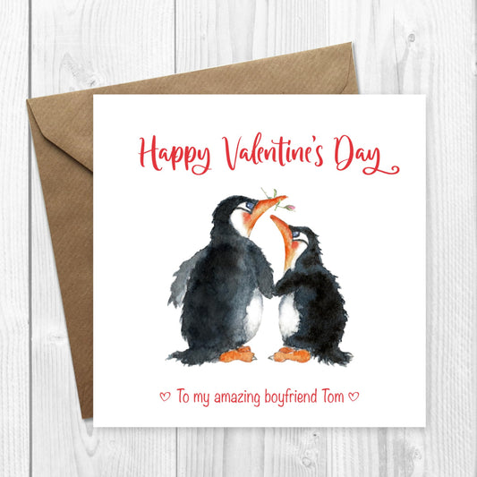 A personalised Valentine's Day card with a watercolor painting of two cute penguins, one giving a kiss to the other, with the text 'Happy Valentine's Day' and 'To my amazing boyfriend'