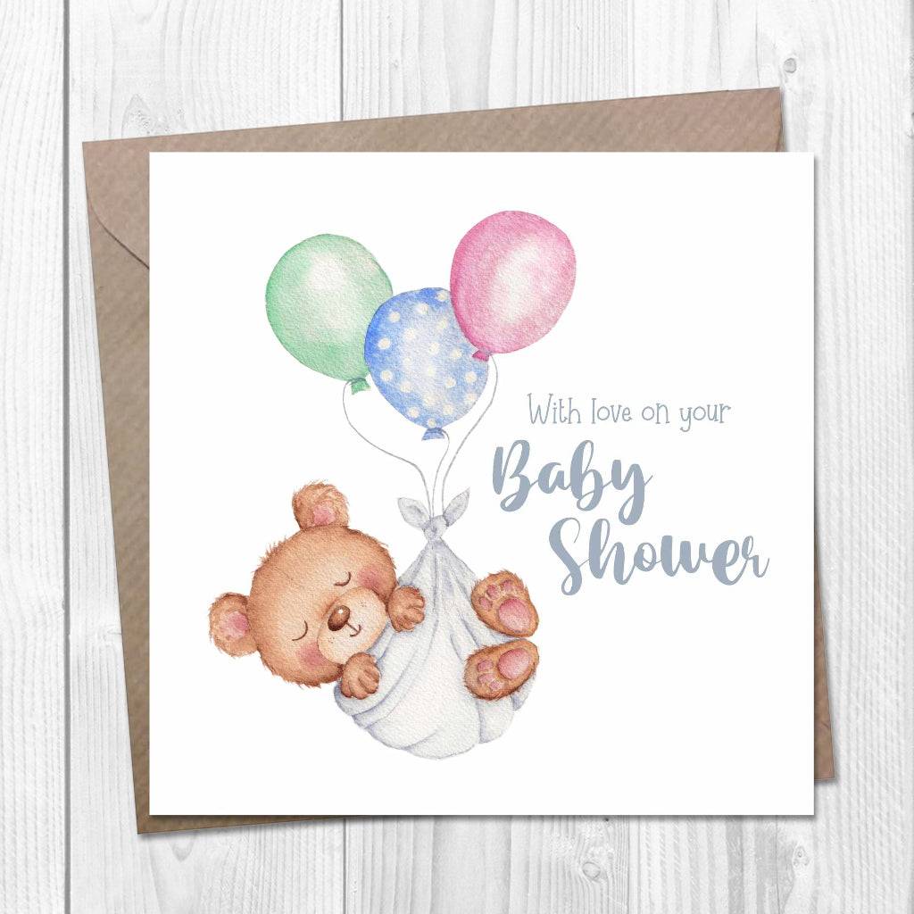 Baby shower card with a teddy bear and balloons on a wooden surface