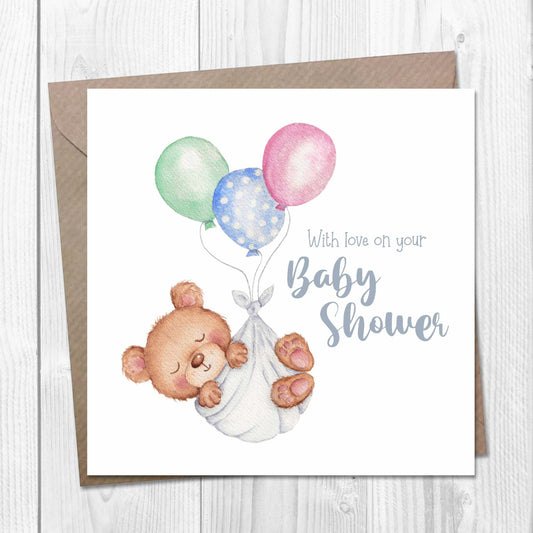 Baby shower card with a teddy bear and balloons on a wooden surface
