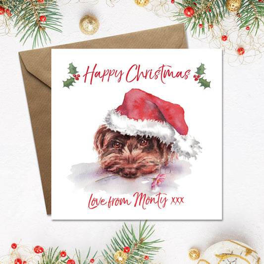 Personalised Happy Christmas card with a cute brown cockerpoo on the front, wearing a santa hat and holding a flower in his mouth. The dog's name is printed underneath