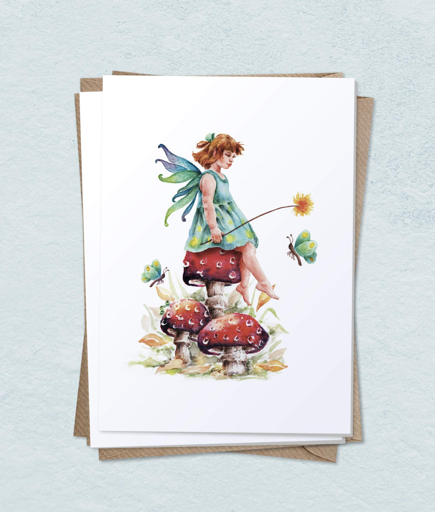 A greeting card with a pretty fairy sitting on a toadstool with butterflies