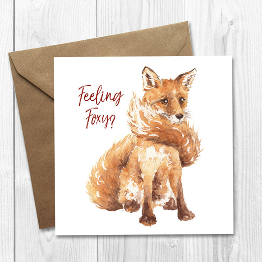 A greeting card with a watercolor illustration of a red fox, with a brown envelope. The text on the card reads 'Feeling Foxy?