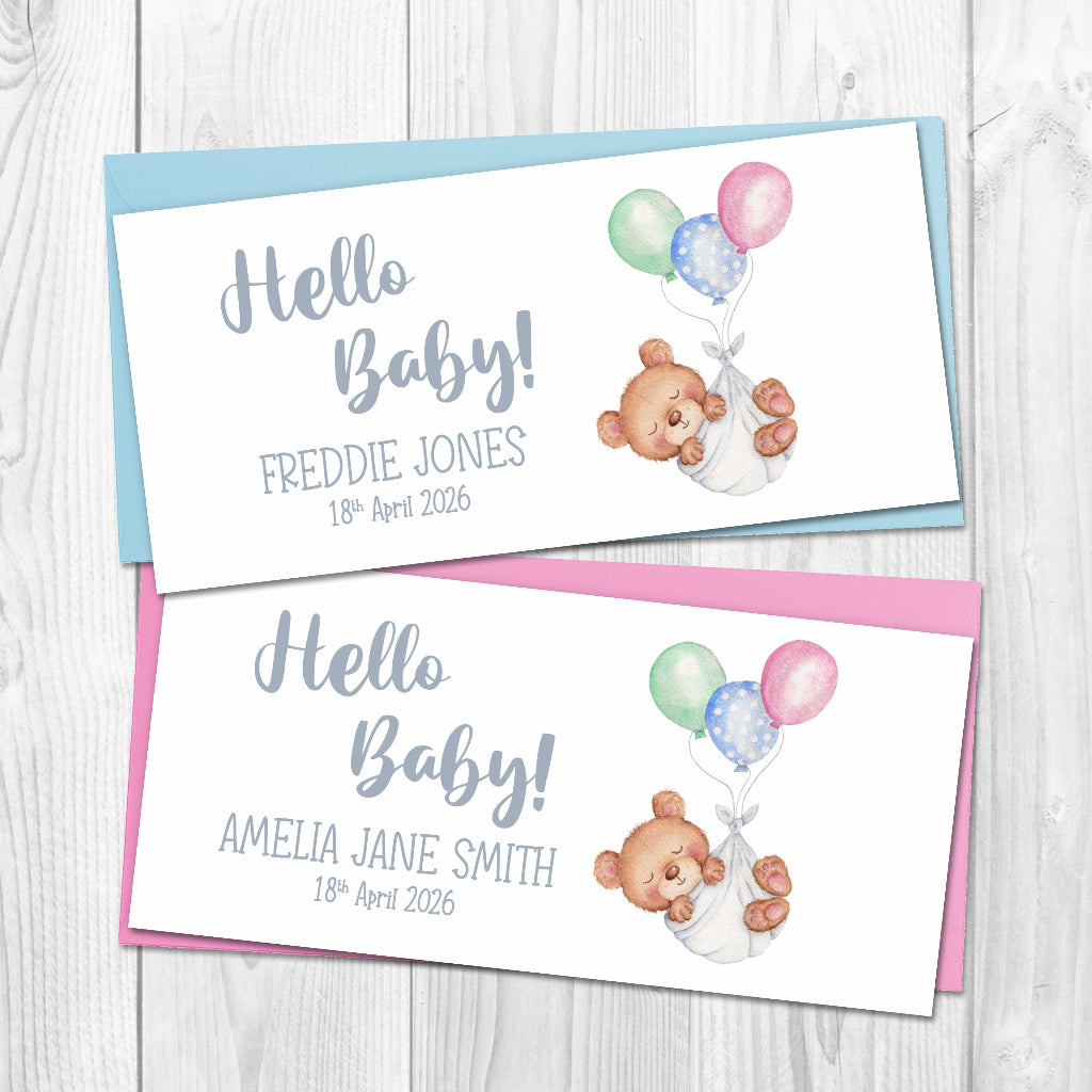 Two Hello Baby money wallet cards with teddy bear and balloons design on a wooden surface. Pink and blue envelopes