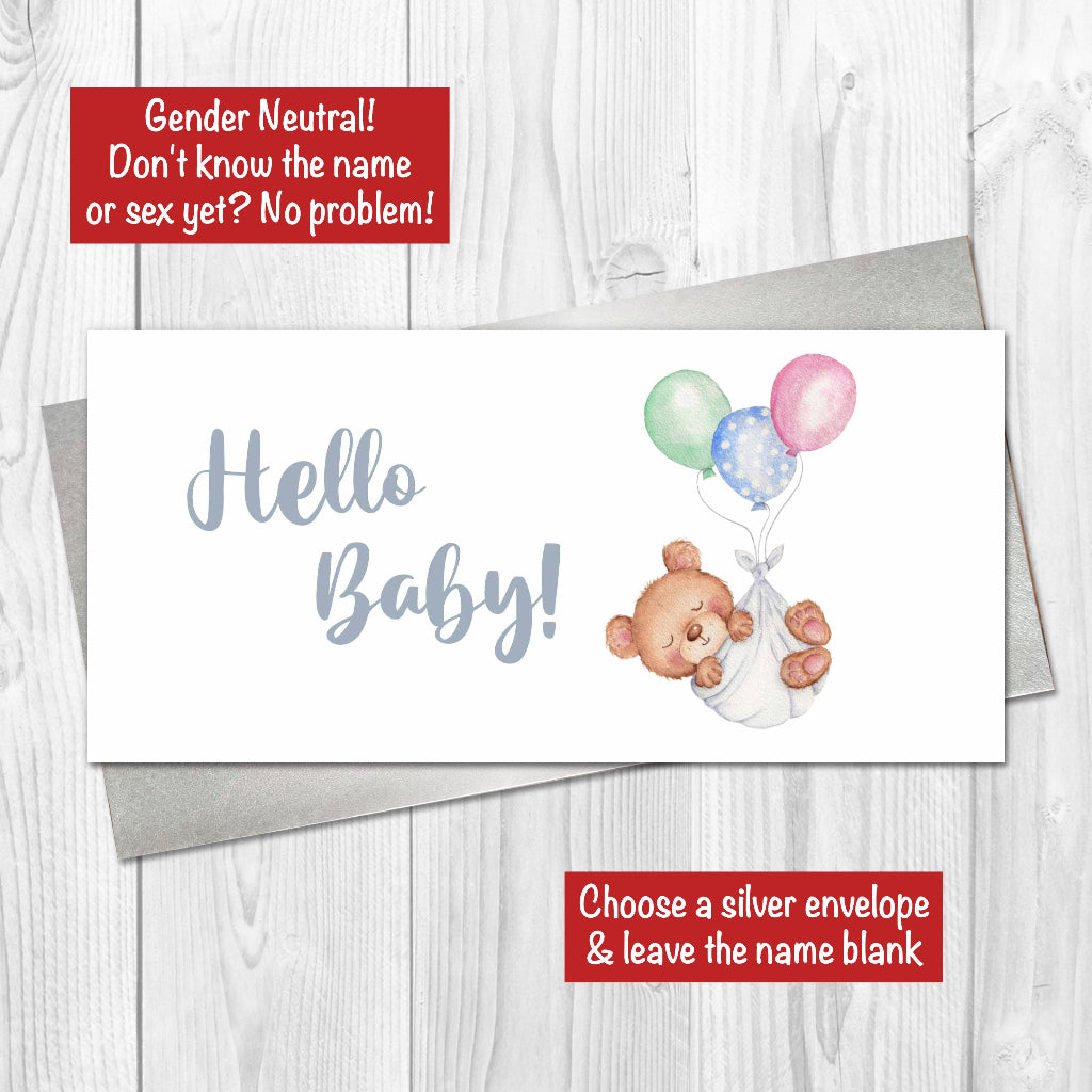 Gender neutral Hello Baby card with teddy bear and balloons and silver envelope on a wooden surface