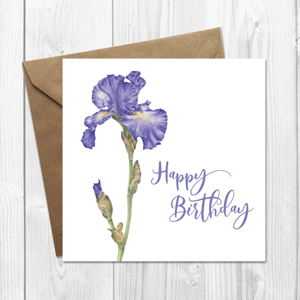 Greeting card with purple iris illustration and 'Happy Birthday' text on a wooden surface