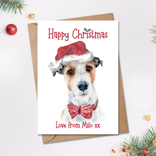 Happy christmas card with a white and tan wire haired jack russell terrier wearing a santa hat and red bow tie. The card is personalised on the front with the dog's name