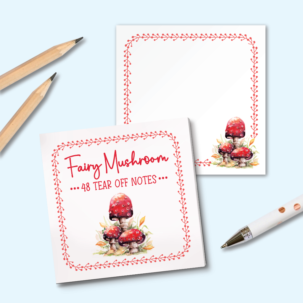 A set of square tear-off notes with a red border and a watercolor illustration of red mushrooms, shown on a light blue background with two pencils and a white pen as props.