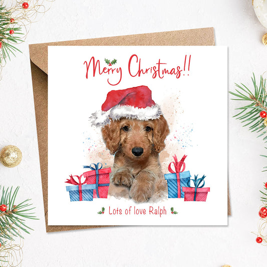 Personalised merry christmas card from the dog with a cute cockerpoo puppy in a santa hat surrounded by presents on the front.