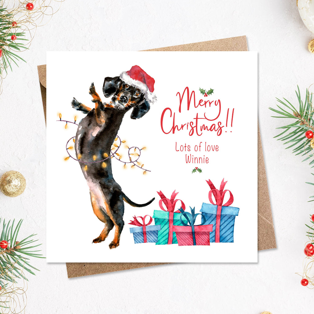 Christmas card with a funny sausage dog in a santa hat partying with fairy lights and xmas presents  around him. The card is personalised from the dog with his name